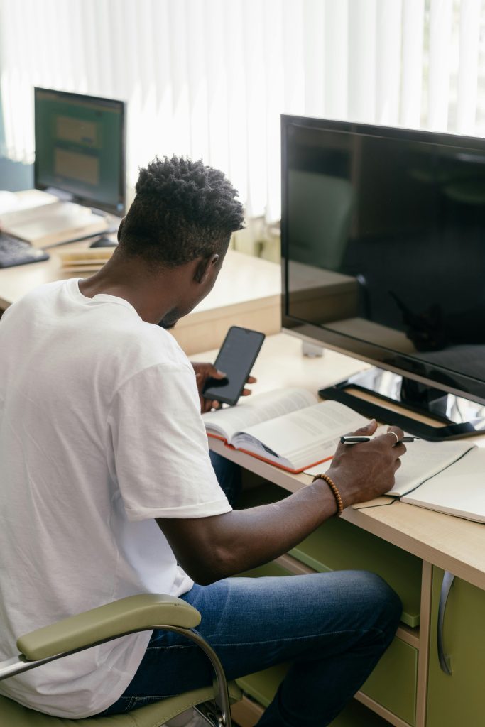 A focused student studies in a classroom using a smartphone and book, highlighting modern learning.